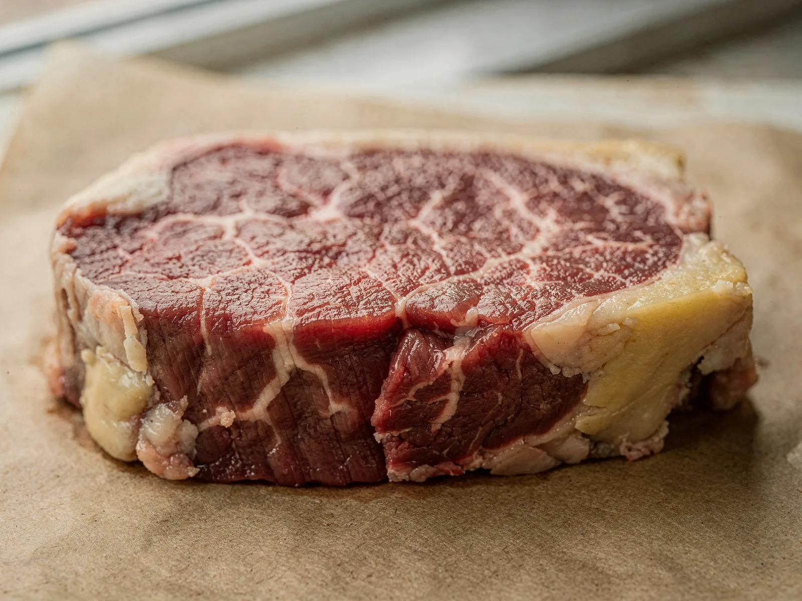 Raw grass-finished steak showing deep red muscle and cream-colored fat